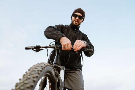 Young focused sportsman checking bicycle's breaks while working out outdoors