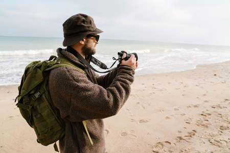 Focused photographer in sunglasses taking photo on digital camera on beach