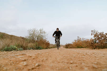 Young focused sportsman riding his bicycle while working out in nature
