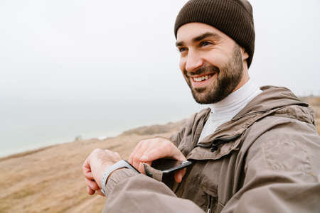 Happy handsome man using smartwatch and cellphone while working out in nature