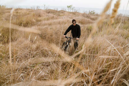 Happy unshaven guy in sunglasses walking with his bicycle outdoorsの写真素材
