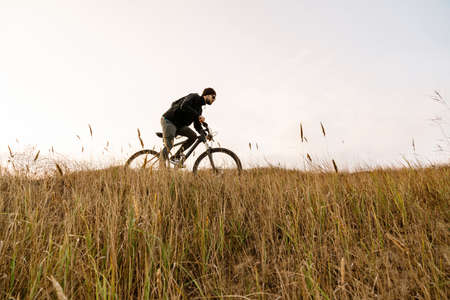 Handsome unshaven guy in sunglasses riding his bicycle outdoorsの写真素材