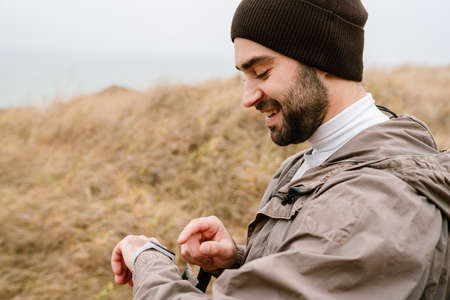 Happy handsome man smiling and using smartwatch while working out in natureの写真素材