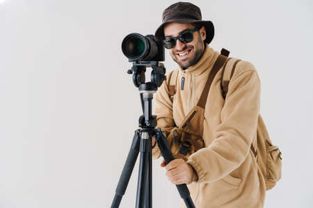 Joyful young photographer taking photo on digital camera isolated over white background