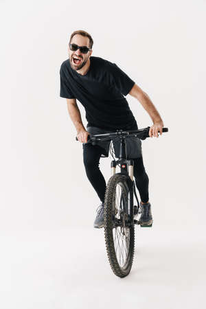 Excited young sportsman in sunglasses riding his bicycle isolated over white backgroundの写真素材