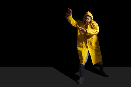 Unhappy man in raincoat grimacing and gesturing on camera isolated over black backgroundの写真素材