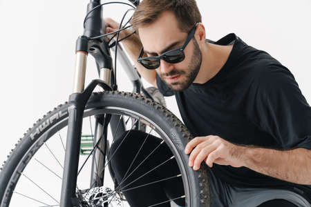 Serious handsome rider man repairing his bike wheel isolated over white backgroundの写真素材