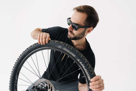 Serious handsome rider man repairing his bike wheel isolated over white backgroundの写真素材