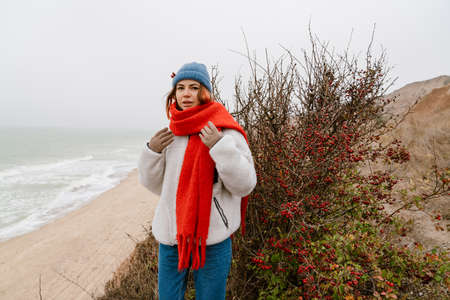Lovely young woman wearing warm clothes walking at the beach