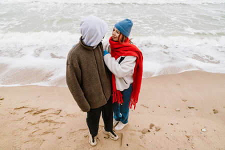 Lovely young multiethnic couple cuddling at the beach, wearing warm clothesの写真素材