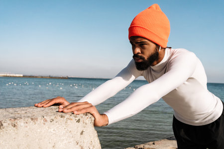 Athletic african american sportsman in earphones doing exercise while working out at beachの写真素材