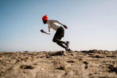 Athletic african american sportsman in earphones running while working out at beachの写真素材
