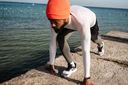 Athletic african american sportsman in earphones doing exercise while working out at beachの写真素材