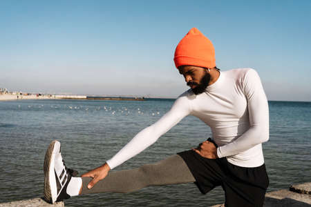 Athletic african american sportsman in earphones doing exercise while working out at beachの写真素材