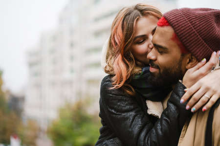Multinational beautiful joyful couple kissing and hugging at city streetの写真素材