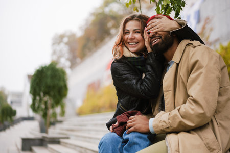 Multinational beautiful lovely couple smiling together while sitting on city streetの写真素材