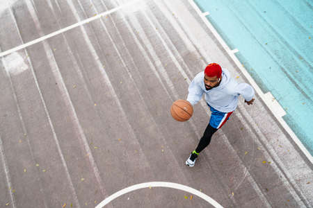 Bearded african american guy in earphones playing basketball at playground outdoorsの写真素材