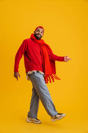 Excited happy african man wearing scarf walking isolated over yellow background, full lengthの写真素材