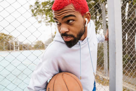 Bearded african american guy in earphones playing basketball at playground outdoors