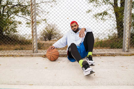 Bearded african american guy sitting with basketball at playground outdoors