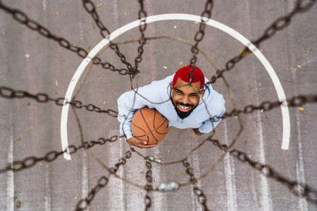 Smiling african american guy in earphones playing basketball at playground outdoors