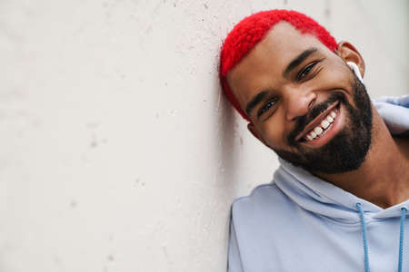 Happy african american guy in wireless earphones smiling and looking at camera outdoorsの写真素材
