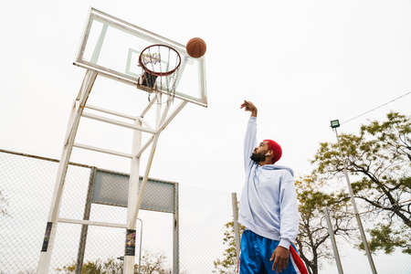 Bearded african american guy in earphones playing basketball at playground outdoors