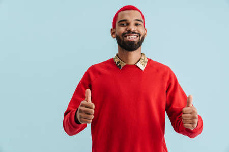 Excited happy african man wearing scarf looking camera isolated over yellow background, thumbs upの写真素材