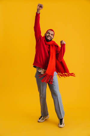 Excited happy african man wearing scarf celebrating isolated over yellow background, full lengthの写真素材