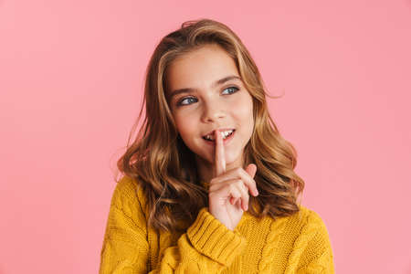 Happy beautiful blonde girl smiling and showing silence gesture isolated over pink background