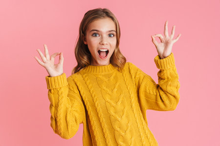 Excited beautiful blonde girl showing ok sing on camera isolated over pink backgroundの写真素材