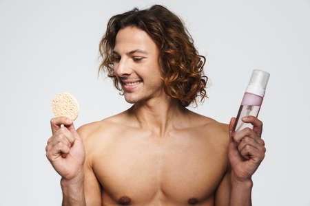 Happy shirtless guy posing with cosmetic sponge and cleansing foam isolated over white background