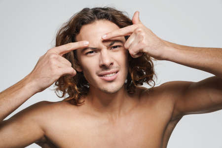 Displeased shirtless guy squeezing pimple on his face isolated over white backgroundの写真素材