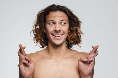 Happy shirtless guy posing with fingers crossed for good luck isolated over white backgroundの写真素材
