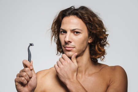 Serious shirtless handsome guy posing with razor isolated over white backgroundの写真素材