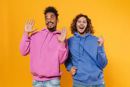 Two joyful men friends dancing isolated over yellow background, having funの写真素材