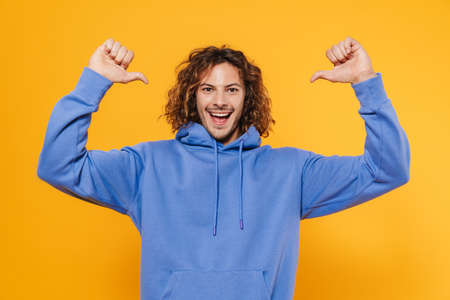 Cheerful young man posing isolated over yellow background, pointing at himselfの写真素材