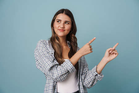 Happy casual woman pointing finger away isolated on a blue backgroundの写真素材