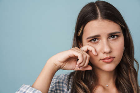 Close up of an upset cute girl wiping tears isolated over blue background