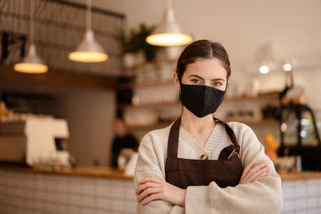 Woman business owner and barista wearing face mask after reopening coffee shop, arms foldedの写真素材