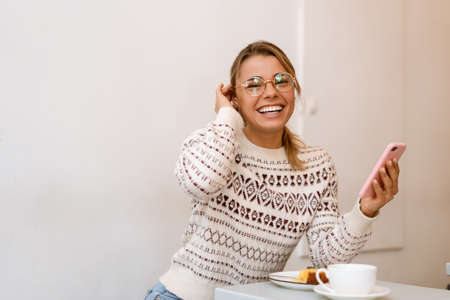 Smiling attractive woman using mobile phone while having lunch at the cafe indoorsの写真素材