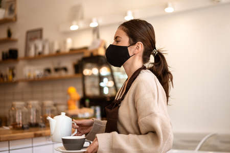 Waitress in a medical protective mask serves coffee in the cafeの写真素材
