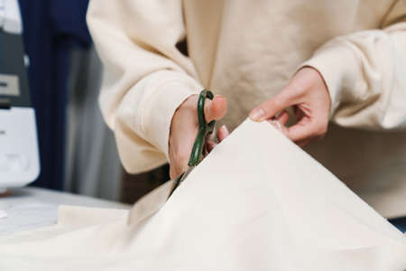 Caucasian nice girl seamstress cutting fabric while working in atelierの写真素材