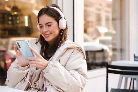 Young woman sitting in the coffee shop, listening to music and holding a smartphone, texting