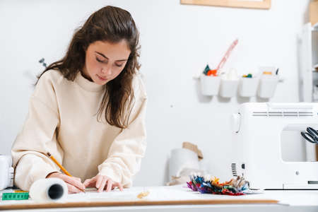 Focused nice brunette girl seamstress writing while working in atelier