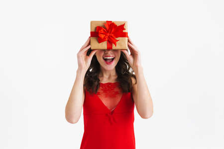 Happy charming girl wearing red dress making fun with gift box isolated over white background