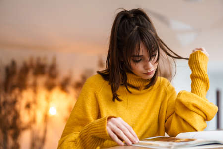 Charming beautiful focused girl reading book while sitting in cafe indoorsの写真素材