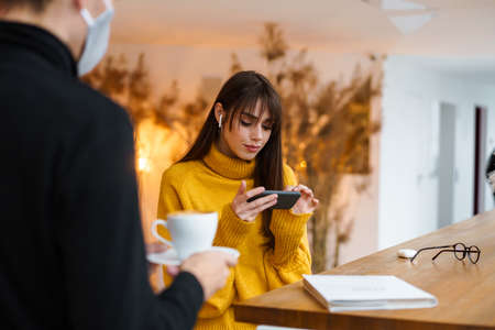 Charming focused girl in earphones at using smartphone at cafe indoors