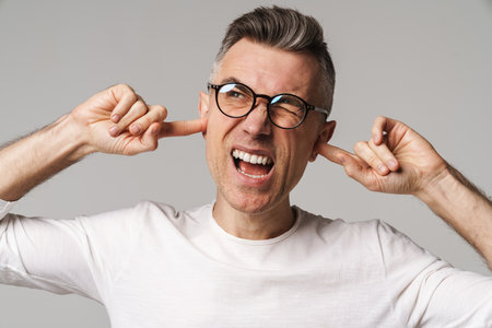 Irritated upset man blocking ears isolated over gray backgroundの写真素材