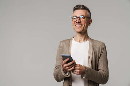 Smiling attractive smart looking man using mobile phone isolated on gray backgroundの写真素材